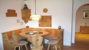 Uma mesa redonda de madeira com cadeiras, um lustre pendurado, armários de madeira e um relógio na parede.