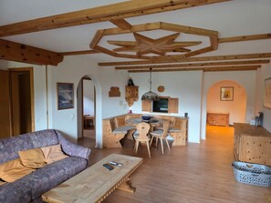 Ein gemütliches Wohnzimmer mit einer hölzernen Bank, einer Couch und einem Essbereich mit Tisch und Stühlen.