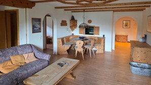 Uma sala de estar acolhedora com um sofá, uma mesa de centro de madeira e um espaço de jantar com uma mesa redonda e cadeiras.