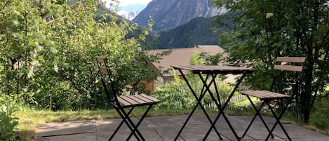 A patio with two tables and chairs, surrounded by greenery and a mountain view.