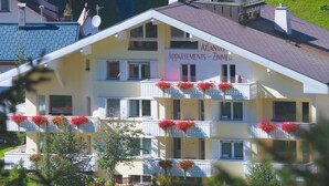 A multi-story building with balconies adorned with flowers, labeled 'Atlantis Apartments Zimmer'. - Atlantis Apartments by MEIN SAMNAUN – MOUNTAIN HOMES, (Samnaun-Ravaisch) by Interhome (Samnaun-Ravaisch)