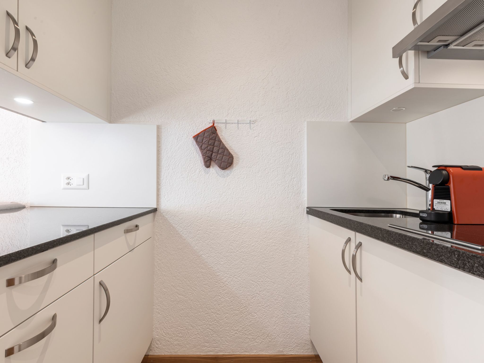 A kitchen with white cabinets, a black countertop, and a red coffee machine.