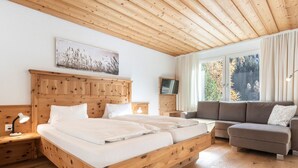 A wooden bedroom with a bed, a sofa, a TV, and a window with curtains.