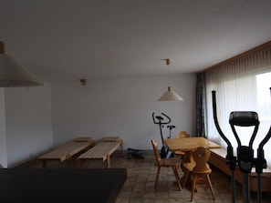 Ein Zimmer mit einem Holztisch, Bänken, einem Stehpult und Trainingsgeräten.