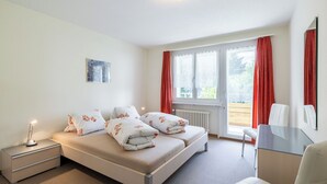 A bedroom with a bed, bedside tables, a desk, and a window with curtains. - HÄMMIG, (Scuol) by Interhome (Scuol)