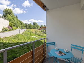 A balcony with a view of a road and greenery, a table with chairs, and a magazine. - HÄMMIG, (Scuol) by Interhome (Scuol)