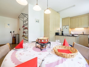 A dining area with a round table set for four, a kitchen in the background, and a coat rack with hangers. - HÄMMIG, (Scuol) by Interhome (Scuol)