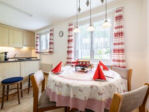 Un coin repas avec une table dressée pour quatre personnes, des chaises, une horloge et une fenêtre avec des rideaux.