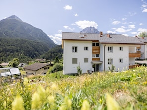 A two-story building with a flat roof, surrounded by a lush green landscape and mountains in the background. - HÄMMIG, (Scuol) by Interhome (Scuol)