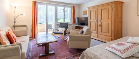 Une pièce bien éclairée, avec un lit, un canapé, une table à manger et un téléviseur. On y trouve une grande armoire en bois et une fenêtre avec des rideaux.