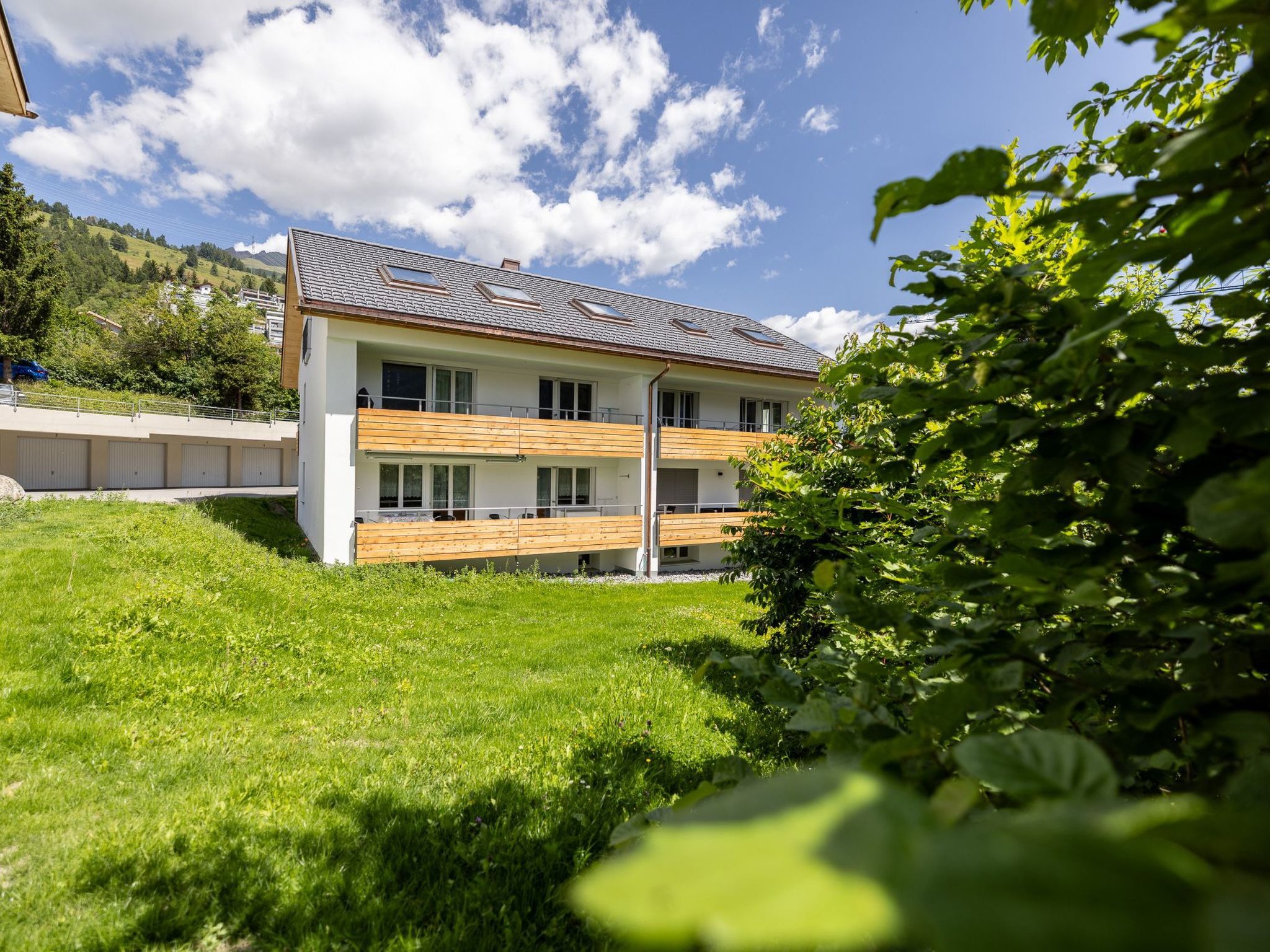 Une maison moderne à deux étages, dotée d’un toit en pente, de grandes fenêtres et d’une terrasse en bois.