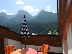 A balcony with a table, chairs, and a striped umbrella overlooking a mountainous landscape. - Via da Pedra Grossa 427A, (Scuol) by Interhome (Scuol)