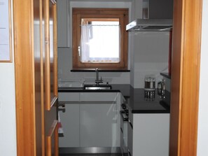 A compact kitchen with a window, a sink, a stove, and cabinets. - Via da Pedra Grossa 427A, (Scuol) by Interhome (Scuol)