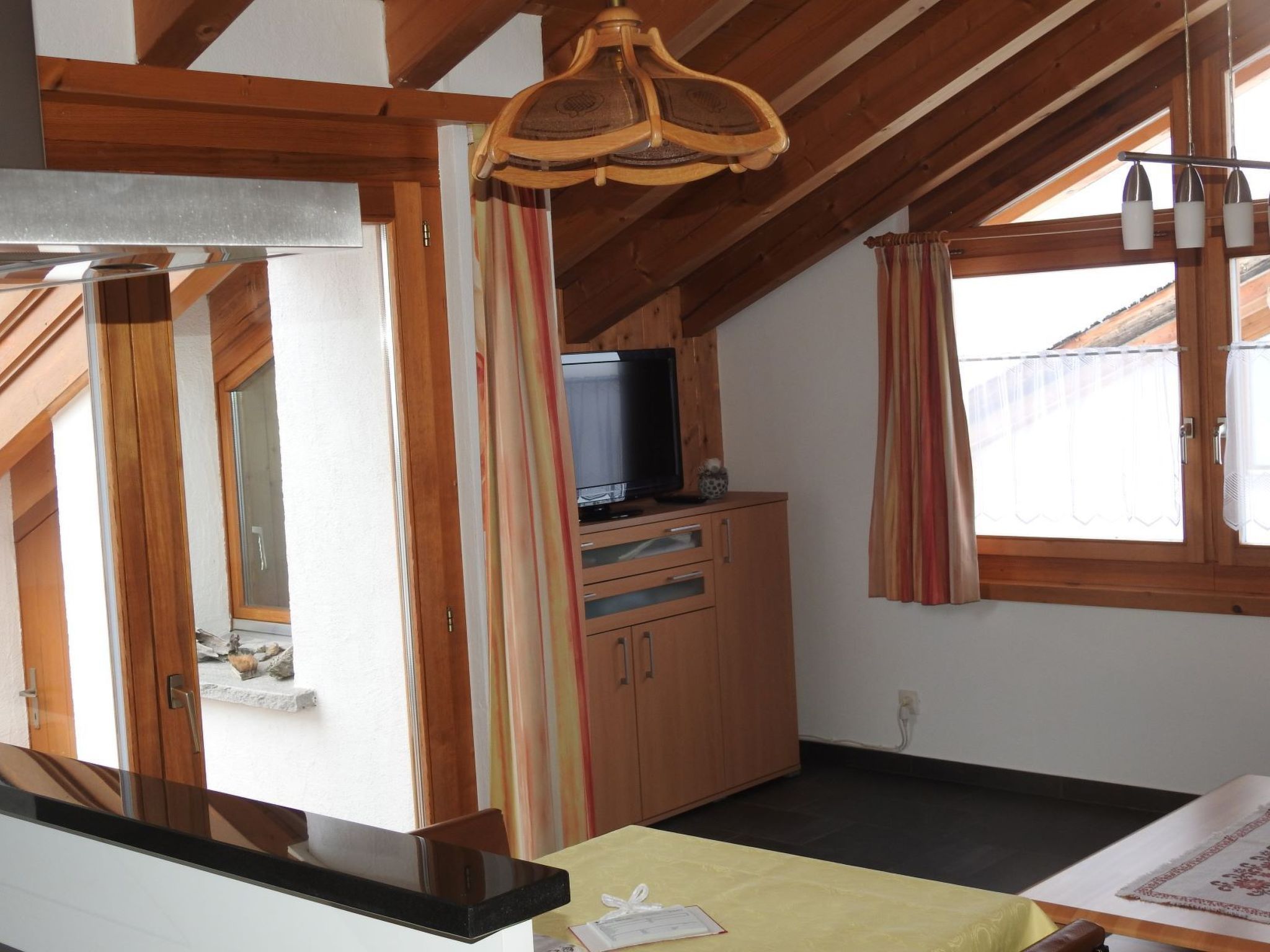 Une pièce avec un plafond en bois, un téléviseur posé sur un meuble et une fenêtre avec des rideaux.