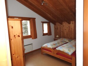 A bedroom with a wooden ceiling, a bed with floral bedding, a window with curtains, and a radiator. - Via da Pedra Grossa 427A, (Scuol) by Interhome (Scuol)