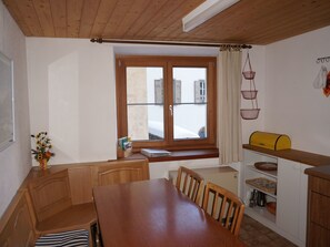 A compact kitchen with wooden cabinets, a dining table, and a window with curtains.