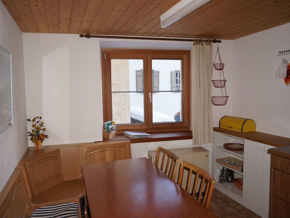 Una cocina compacta con armarios de madera, una mesa de comedor y una ventana con cortinas.