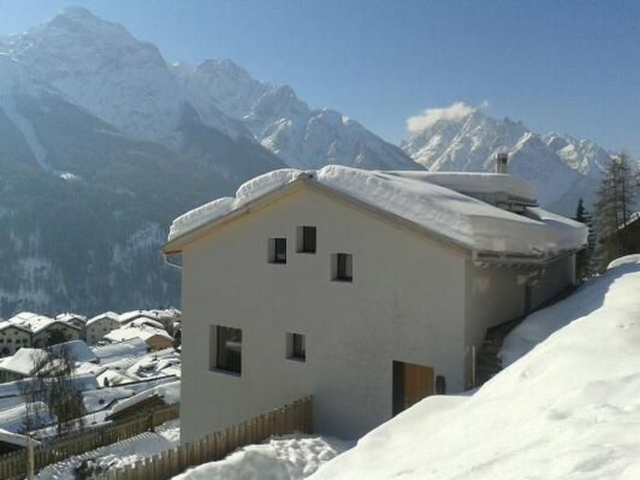 Un edificio cubierto de nieve con una estructura sencilla de un solo piso, rodeado de un paisaje nevado y montañas al fondo.