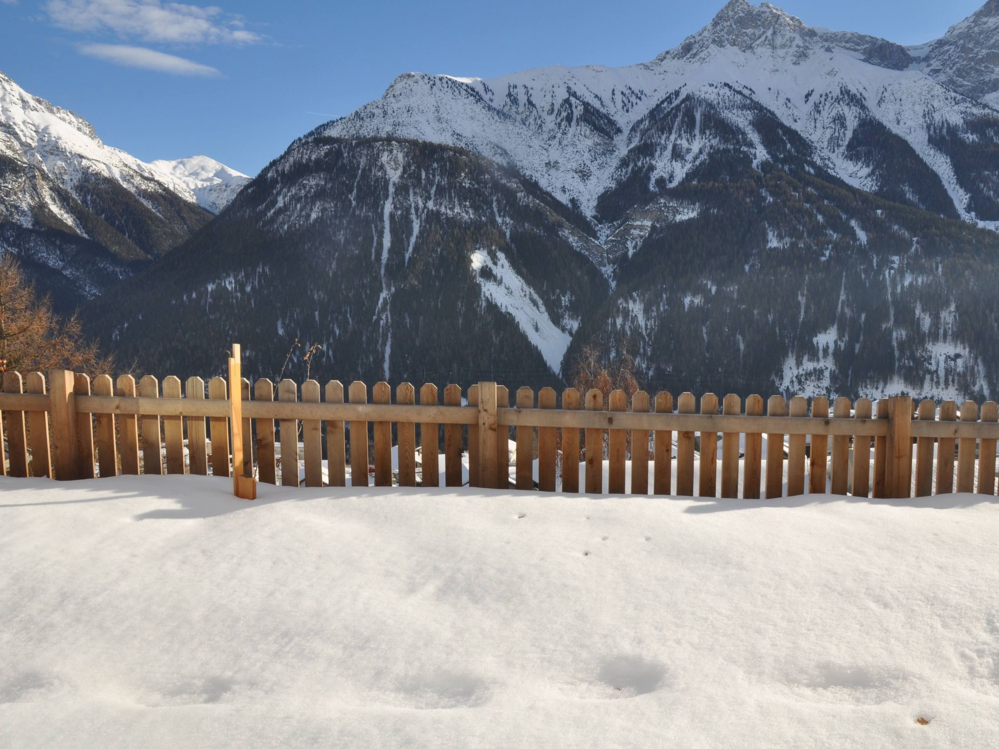 Une clôture en bois dans un paysage enneigé, avec des montagnes en arrière-plan.
