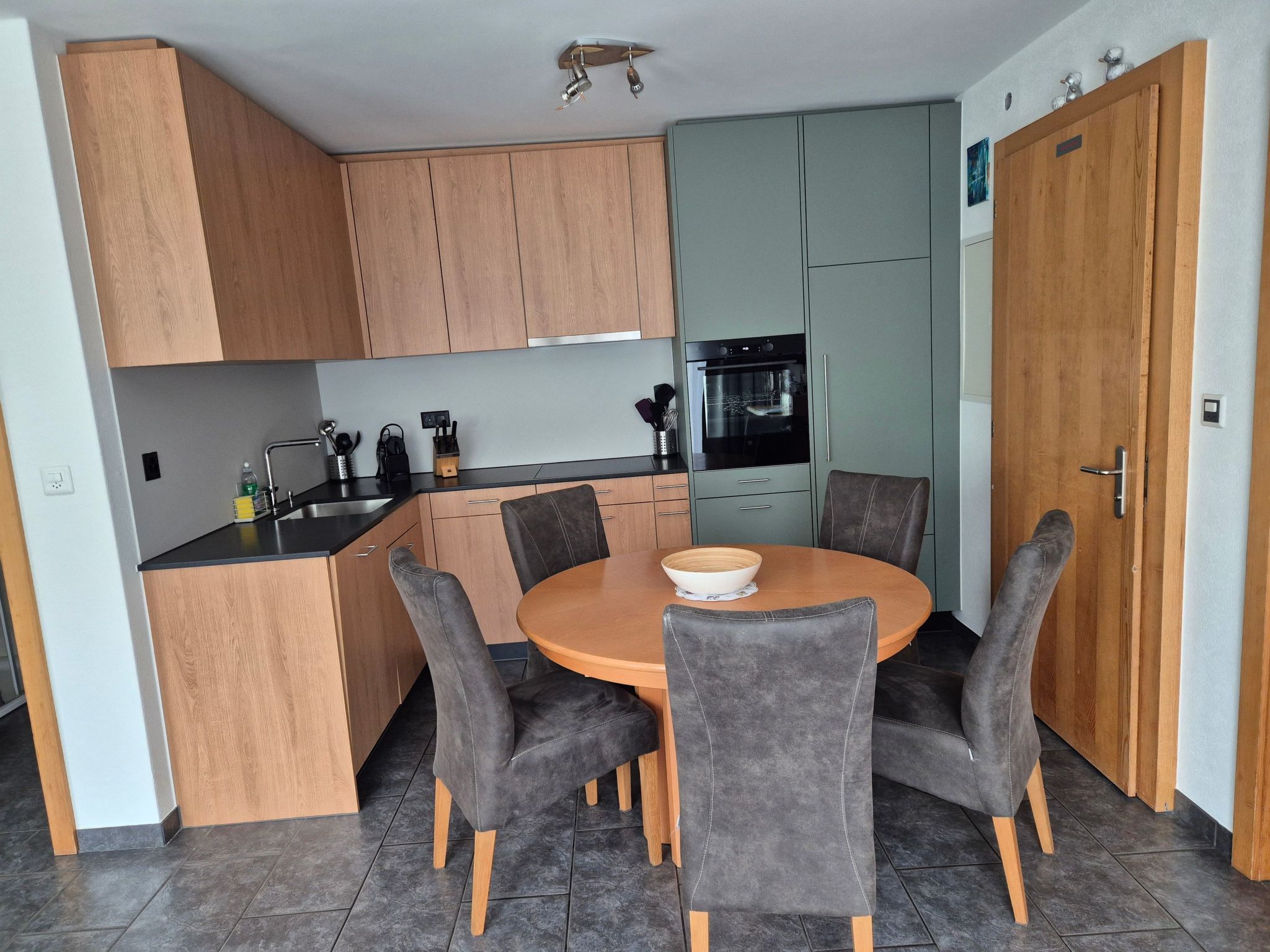 A compact kitchen with wooden cabinets, a dining table with chairs, and a built-in oven.