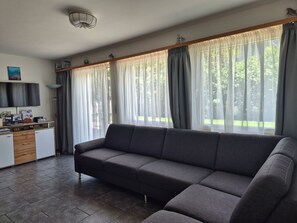 Un salon moderne avec un canapé gris, un téléviseur à écran plat fixé au mur et un coin cuisine doté d’un plan de travail et de placards.