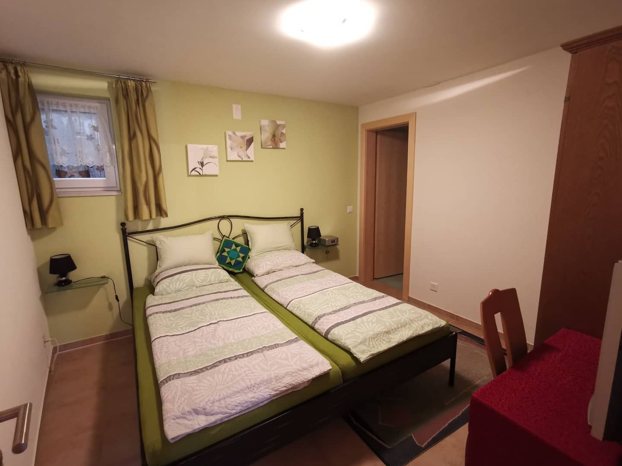 A single-bed room with a green mattress, a bedside table with a lamp, and a window with curtains.