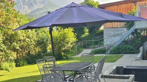 Eine Terrasse mit Tisch und Stühlen, einem Sonnenschirm und Blick auf einen Berg.