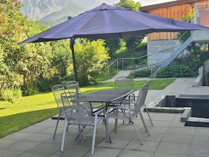 Un patio con una mesa, sillas y una sombrilla, con vistas a una montaña.