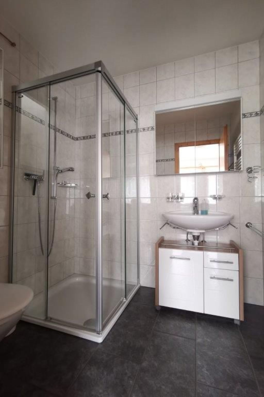Ein Badezimmer mit einer Duschkabine aus Glas, einem weißen Waschbecken mit Spiegel darüber und einem Schrank mit Schubladen.