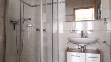 Ein Badezimmer mit einer Duschkabine aus Glas, einem weißen Waschbecken mit Spiegel darüber und einem Schrank mit Schubladen.