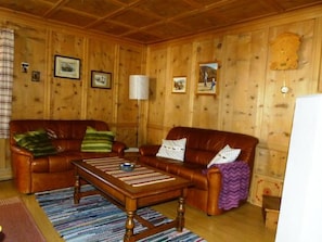 A wooden-paneled room with a brown leather sofa, a wooden coffee table, and a patterned rug. - Melcher Jon & Brigitte - Bauernhaus, (Valchava) by Interhome (Valchava)