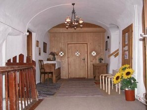Un pasillo con una puerta de madera, un comedor con una mesa y sillas, y una planta en maceta con girasoles.