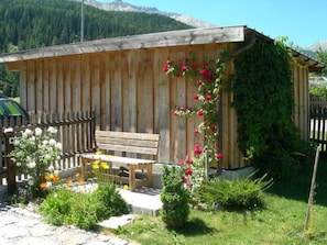 A wooden cabin with a bench, surrounded by a garden with various plants and flowers. - Melcher Jon & Brigitte - Bauernhaus, (Valchava) by Interhome (Valchava)