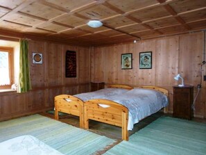 Ein Zimmer mit Holzboden, einem Bett, einem Fenster mit Vorhängen und Bildern in Rahmen an der Wand.