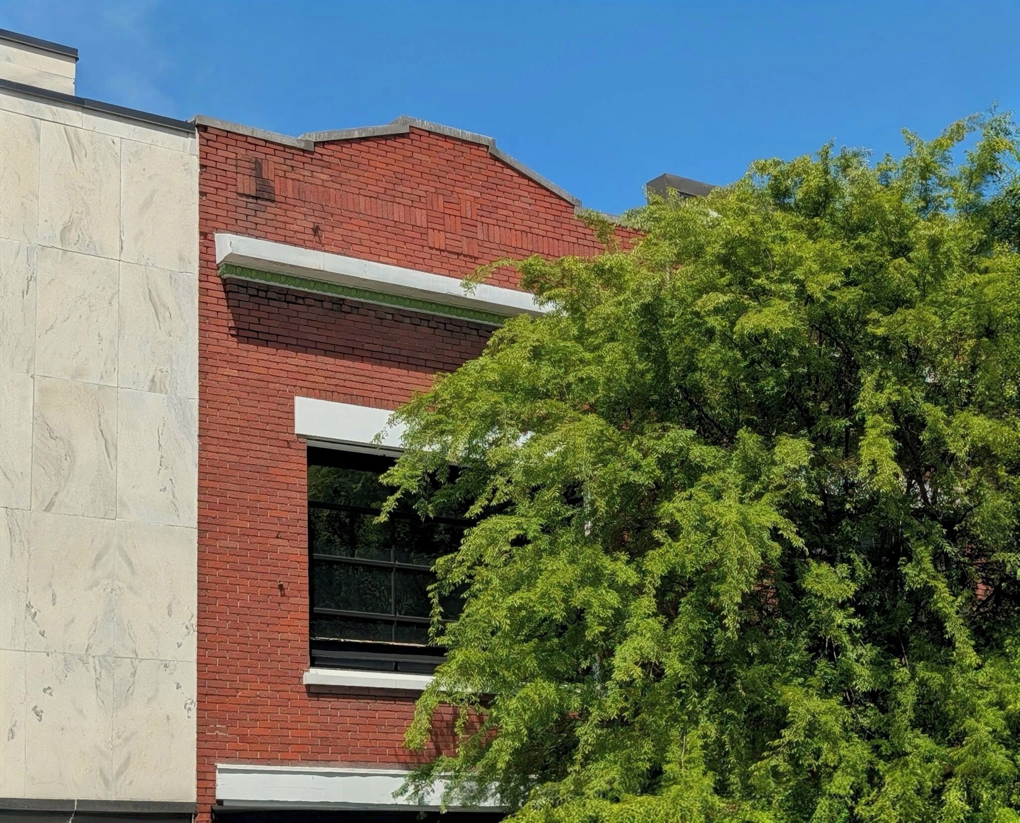 A building with a red brick facade, a large window, and a tree in front.
