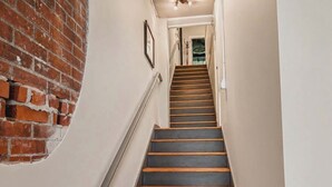 A staircase with wooden steps and a metal handrail, leading to a room with a brick wall and a door. - Huge Historic Loft on State Street!  2 bed - 2 Bath - With view of Downtown (Bristol)