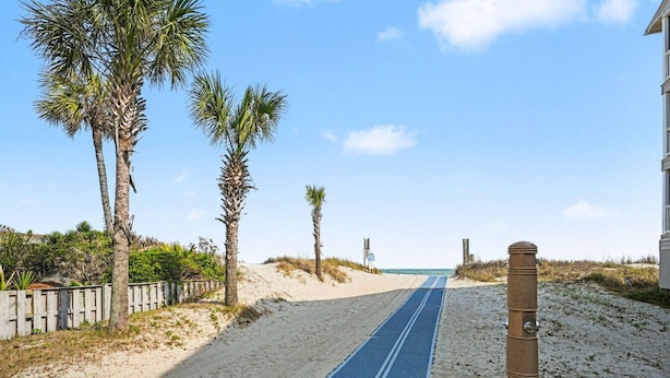 Ein Weg führt zu einem Strand mit Palmen, einem Holzzaun und einer blauen Matte.