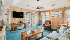 Ein Wohnzimmer mit Fernseher, Deckenventilator, Sofa, Couchtisch und Sessel.