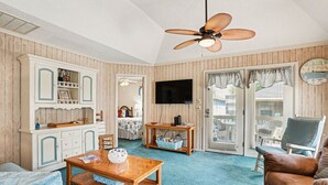 Ein Zimmer mit Deckenventilator aus Holz, einem Fernseher, einer Holzkommode, einem Couchtisch und einem Ledersofa.