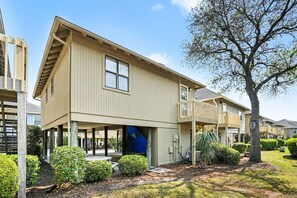 A two-story residential building with a covered garage, a small front yard with shrubs, and a tree. - Nostalgic Beach Cottage. Perfect for Holiday Breaks Unplug near the beach (Myrtle Beach)
