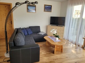 A modern living room with a sofa, a coffee table, a TV, and a large window with curtains. - Fionas 257, (Ftan) by Interhome (Ftan)