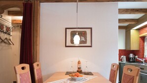 Zona pranzo con tavolo in legno, quattro sedie, un quadro appeso e una cucina sullo sfondo.