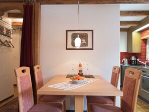 Ein Essbereich mit einem Holztisch, vier Stühlen, einem gerahmten Bild an der Wand und einer Küche im Hintergrund.