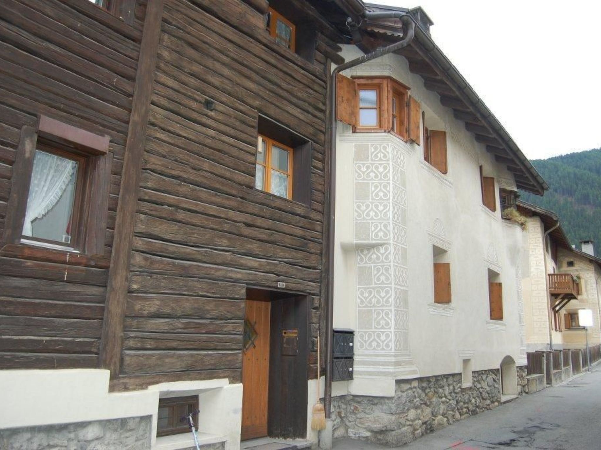 Edifici de fusta tradicional amb fonamentació de pedra, una porta de fusta i una finestra amb cortina.