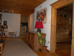 A wooden interior with a kitchen area, a dining table, and a red lamp on a wooden stand.