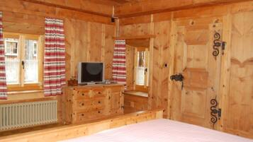 Ein Zimmer mit Holzboden, einem Bett, einem Schminktisch, einem Fernseher und Vorhängen.