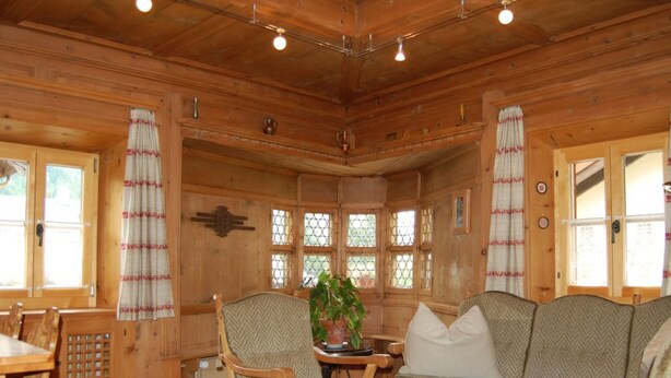 Interior de uma cabana de madeira com uma mesa de jantar, cadeiras, um sofá e um vaso de planta.