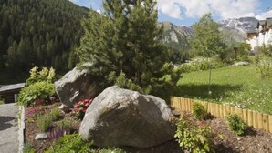 Un paysage montagneux avec une maison entourée d’un jardin agrémenté de grandes roches et de plantes en fleurs.