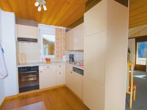 A compact kitchen with wooden cabinets, a built-in oven, and a window with floral curtains. - Atlantis Apartments by MEIN SAMNAUN – MOUNTAIN HOMES, (Samnaun-Ravaisch) by Interhome (Samnaun-Ravaisch)