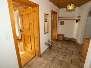 Un pasillo con puertas de madera, un espejo, un pequeño banco y un jarrón con flores.